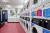 A laundry room with a wall of laundry machines, and seating on the opposite wall.
