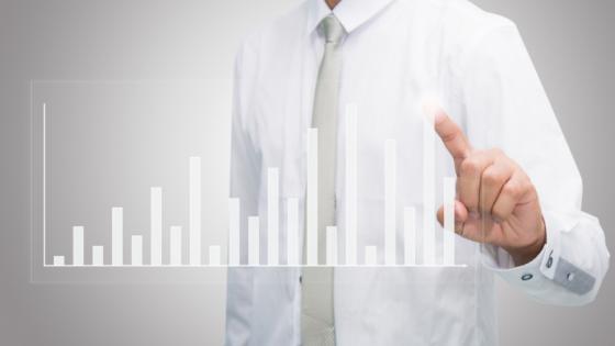 a man in a work shirt and tie pointing to a graph