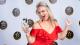 Cheryl Laidlaw is smiling cheerfully with her hands raised in front of a Best Businesswomen Awards backdrop. She is holding the trophy in one hand.