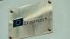 Close-up of a metallic plaque mounted on a light-coloured wall displaying the Erasmus+ logo and name. The rectangular plaque is secured with four visible screws at the corners and features the Erasmus+ text beside the European Union emblem.