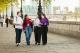 Four university students walk together along a riverside path in central London, chatting and smiling, with city buildings and a bridge visible in the background.