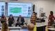 Panellists of the event sit in front of a whiteboard displaying the research centre's mission statement. On the right of the screen, Professor Lilian Miles addresses the audience. To her right, there are Dr Maria Granados and Dr Anne Line Rodriquez.