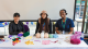 Three females sitting at table with crochet equipment 