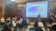 Attendees at the Gender, Tourism and Climate Change sit around tables in front of a projector with "Welcome" "Gender, Tourism and Climate Change Round Table Discussion" displayed on it. Dr Stroma Cole stands at the front. 