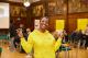 A student smiling at the camera wearing a yellow hoodie and holding up peace signs 