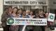 A group of people standing outside of city hall with banners and posters