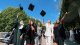 A group of female students wearing graduation robes throwing grad caps 