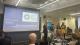 Professor Peter Bonfield delivering a welcome address alongside Professor Lilian Miles, Dr Maria Granados and Professor Dibyesh Anand. They stand to the right of a projector displaying the RCPP logo and the title of the event: Supporting Asylum Seekers and Refugees: A Collaborative Approach