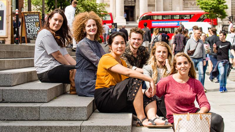 Westminster students sitting on stairs in Central London with red double decker buses in the background