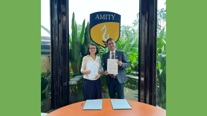 Dr Katalin Illes and colleague from the Amity Group posing for a photo standing up and holding the signed agreements