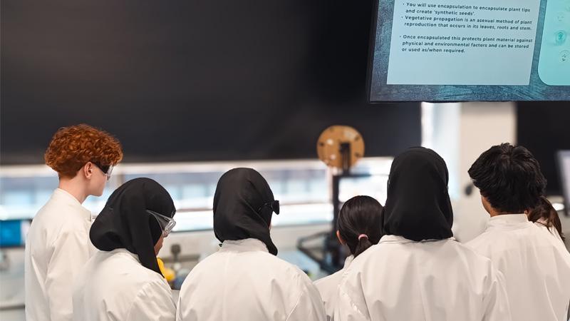Students gathered around a lab bench wearing white lab coats.