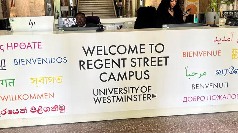 The reception desk at Westminster's Regent Street, which is white and reads WELCOME TO REGENT STREET CAMPUS UNIVERSITY OF WESTMINSTER in black text. The word welcome in a variety of languages surrounds this text in different colours.