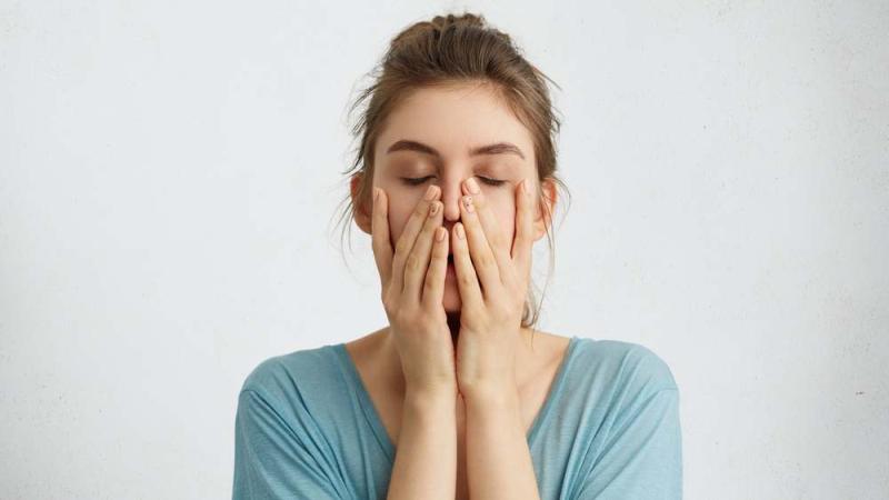 A stressed woman with eyes closed and hands on her face